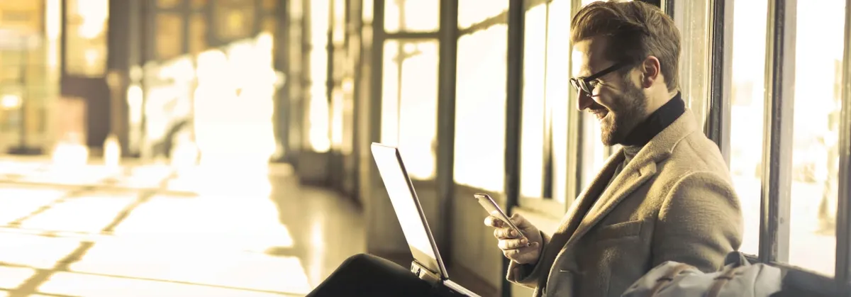 A happy man looks at his phone while working in a hall