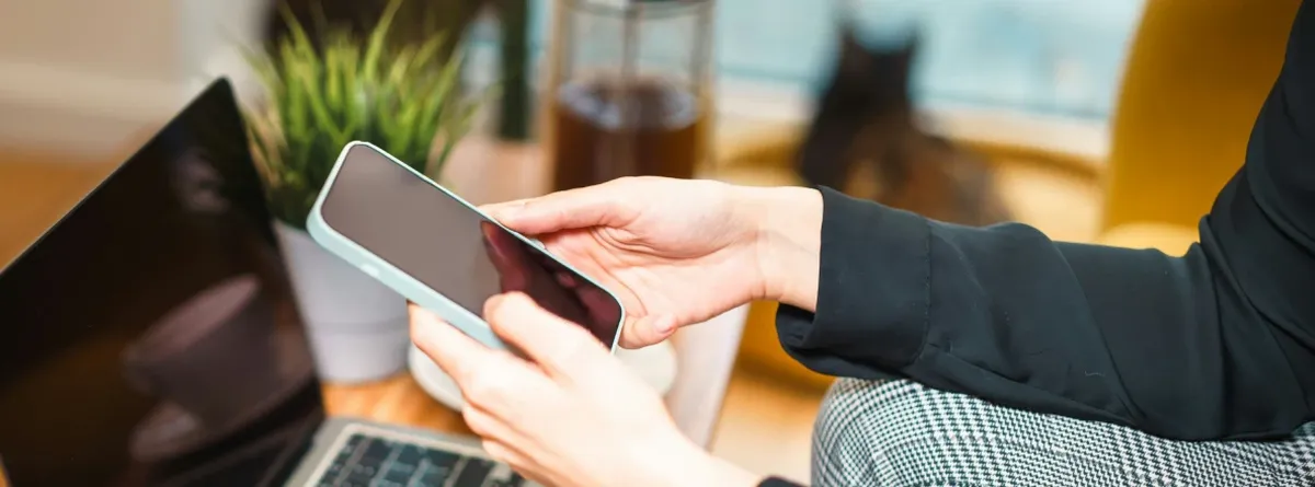 Business Mobile Plans - woman working on her phone while seated in front of laptop