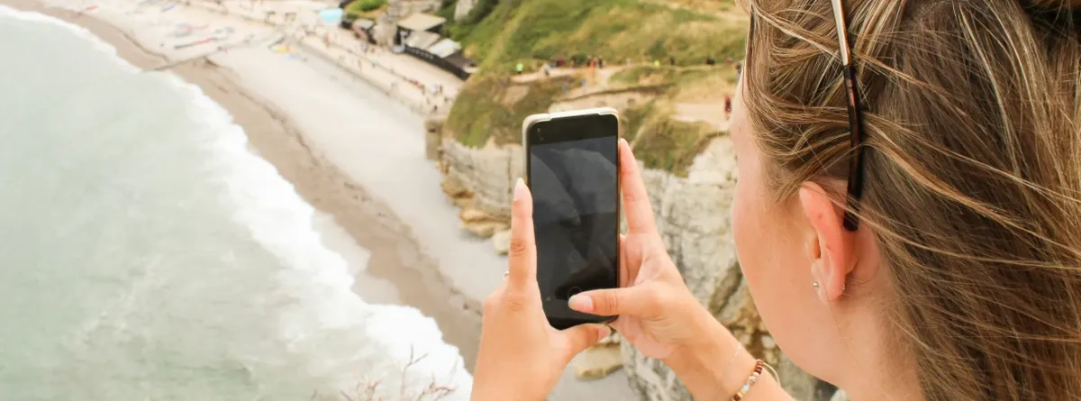 Beyond travel data - woman taking a picture on her mobile phone of a beach landscape below