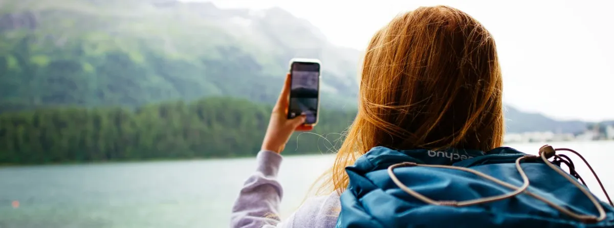 Consumer eSIM Roaming - woman taking a photo of a lake and green hill