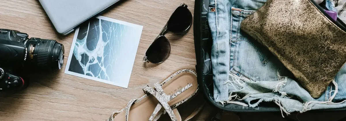 An open suitcase spilling its summer travel contents onto a wooden floor