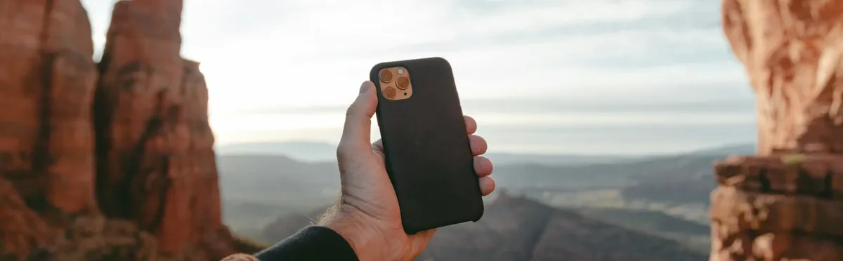 A hand holding an eSIM-enabled smartphone in front of a mountainous landscape