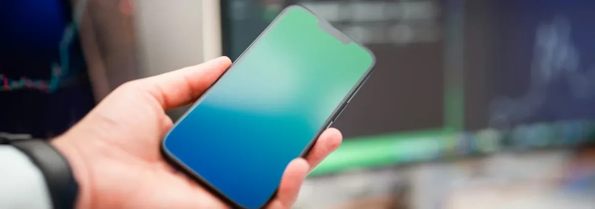 APIs as glue - hand holding a mobile phone in front of a bank of monitors and computers