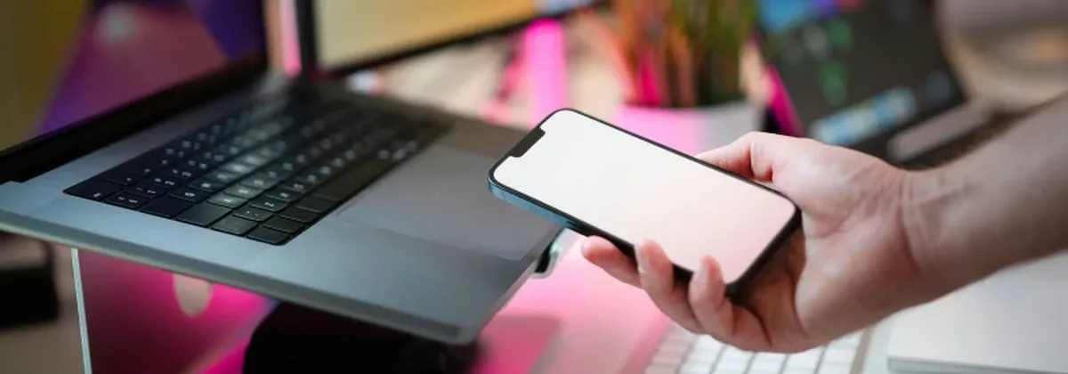 Dynamic Profile Adaptation - hand holding mobile phone while working on a laptop