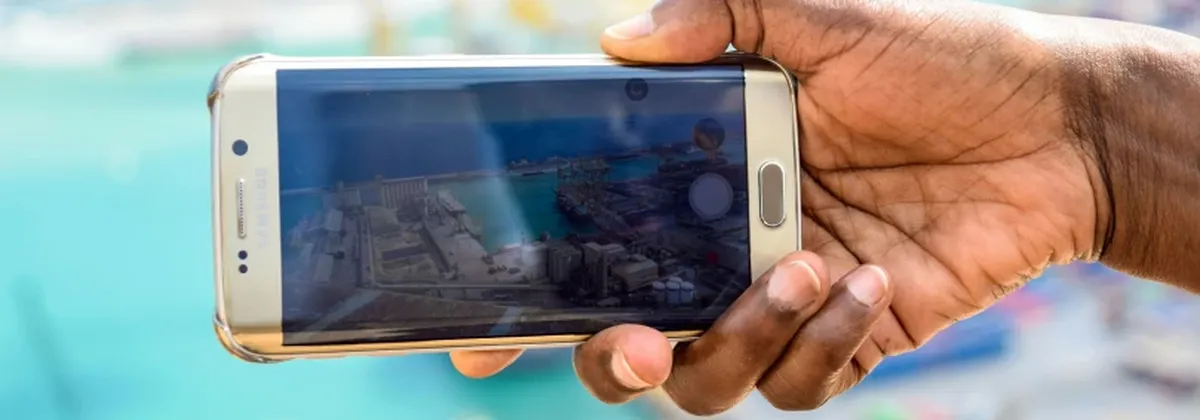 RSP in Emerging Markets - a hand holding a mobile phone against a sunny backdrop and harbour